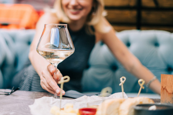 a woman reaching for a glass of white wine on a table with appetizers