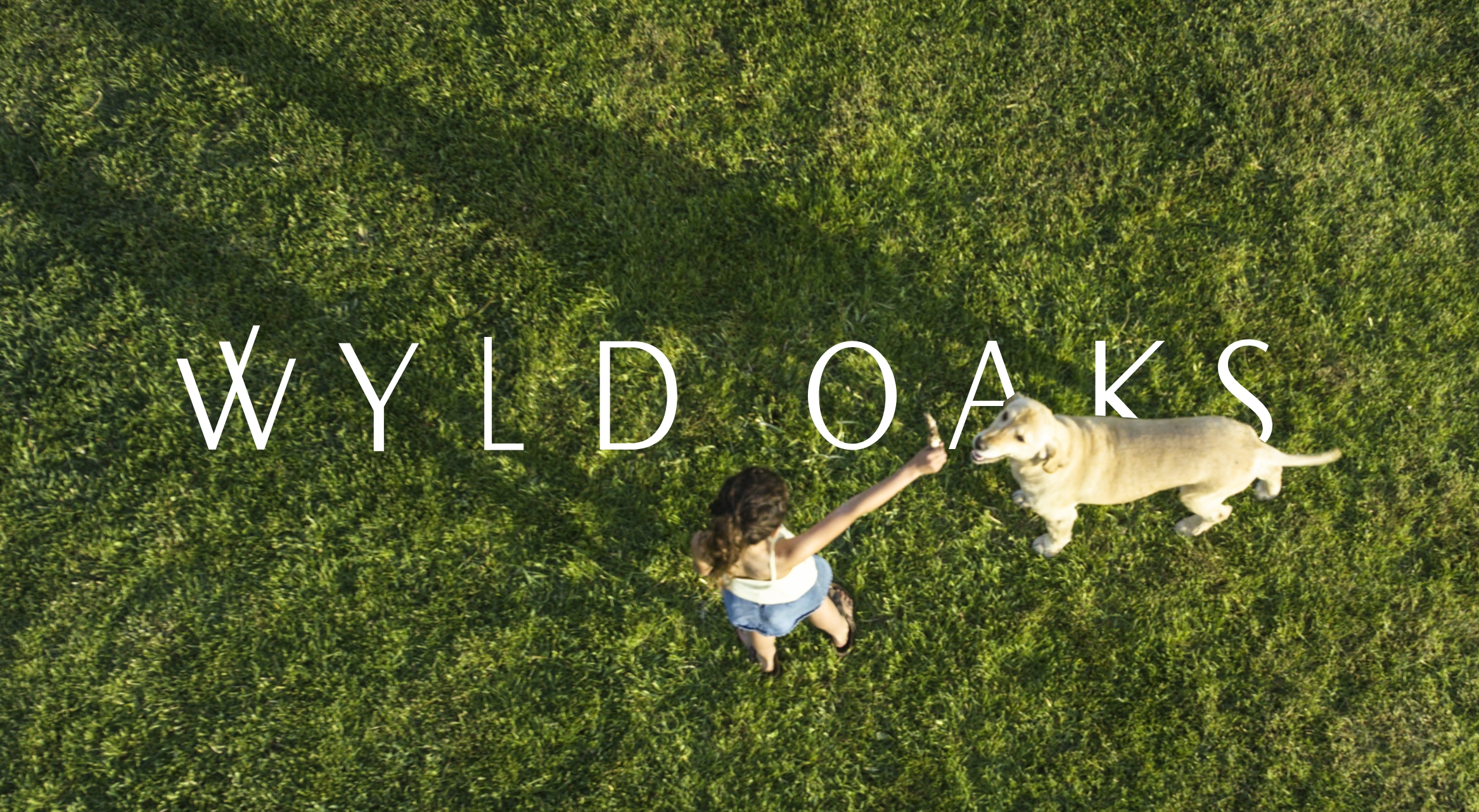 girl playing with her dog with Wyld Oaks logo in the background over the grass