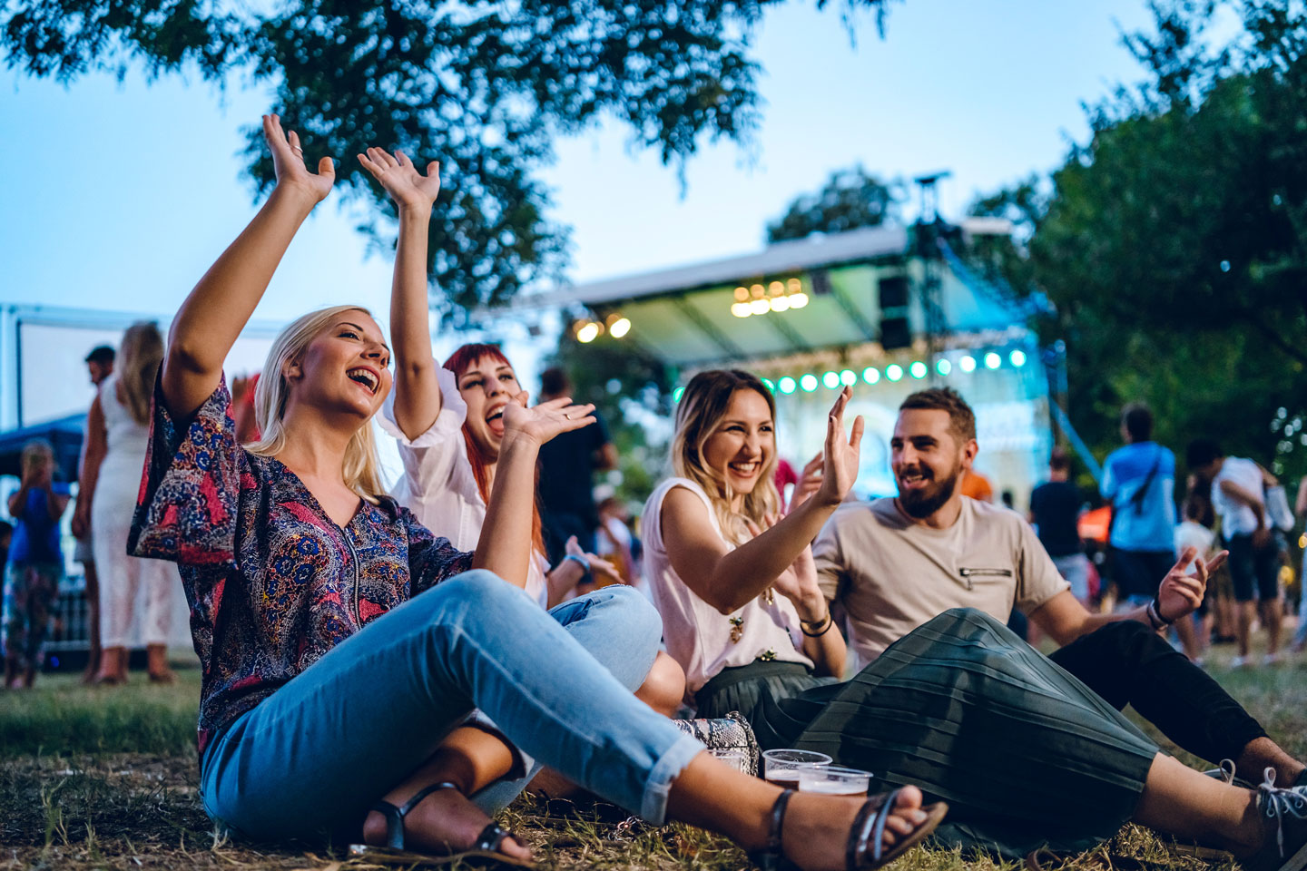 Friends sitting on the grass next to a stage smiling and cheering